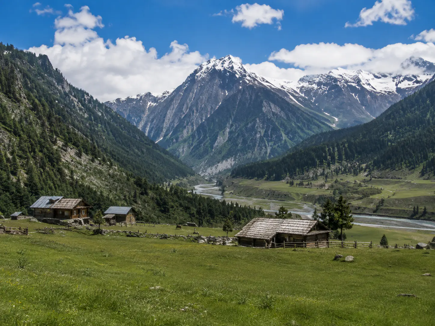 Two hikers following a glacial stream beneath Sonamarg's mountain wall